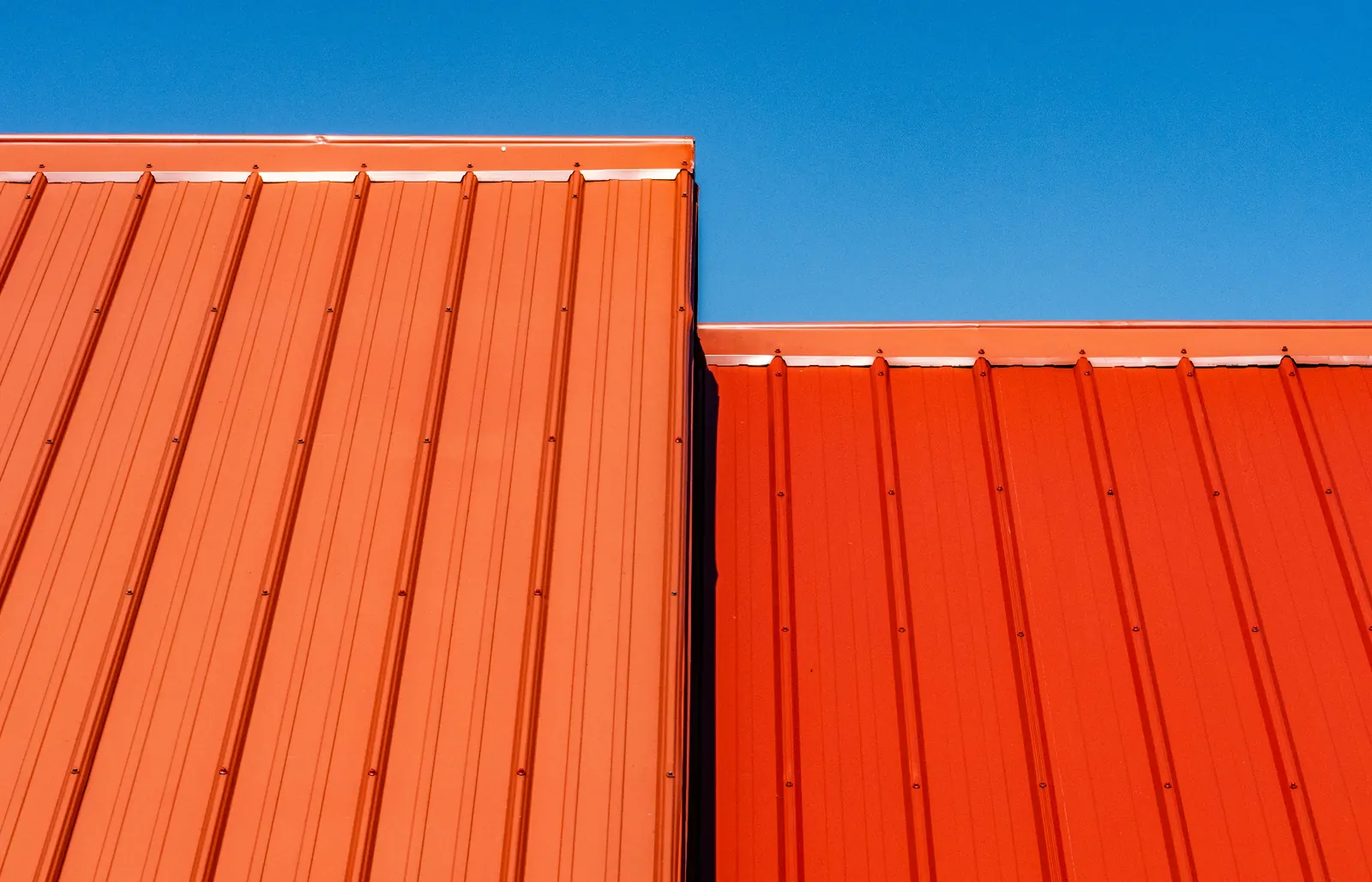 Orange standing seam metal roof panels under a clear blue sky